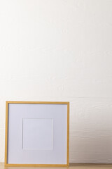 Vertical of empty wooden frame with copy space on table against white wall