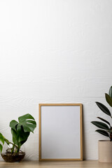 Vertical of empty wooden frame with copy space and plants in pots on table against white wall