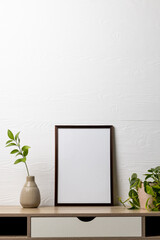 Vertical of black empty frame with copy space and plants in pots on table against white wall
