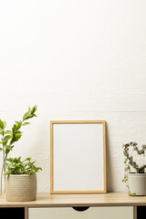 Vertical of empty wooden frame with copy space and plants in pots on desk against white wall