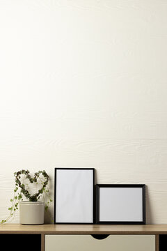 Vertical of two empty black frames with copy space and plant on table against white wall