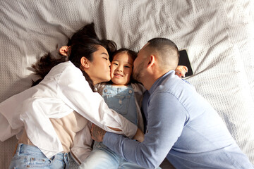 asian mom and dad kiss little baby girl and lie on bed, happy korean family with daughter, concept...