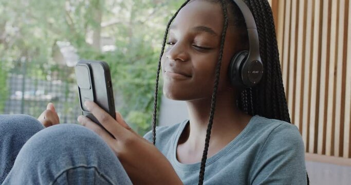 Happy african american teenage girl with headphones listening to music with smartphone