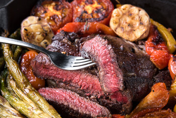 Piece of ribeye steak on a fork with vegetables.
