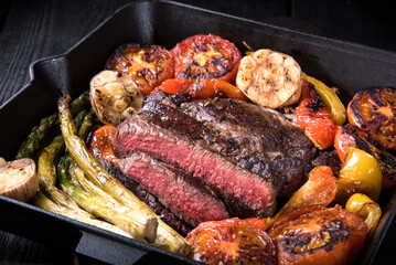 Fried rib eye steak in a cut in a cast iron pan with vegetables.