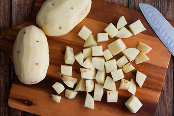 Peeled and Cubed Russet Potatoes on a Wood Cutting Board: Fresh potatoes chopped into small cubes with a kitchen knife and chopping board