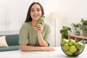 Beautiful woman with bottle of delicious smoothie at table indoors