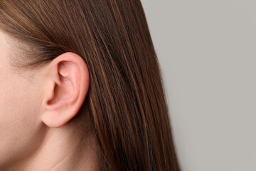 Closeup view of woman against light grey background, focus on ear