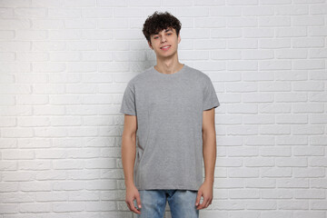 Man wearing gray t-shirt near white brick wall. Mockup for design