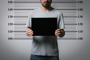Criminal mugshot. Arrested man with blank card against height chart, closeup