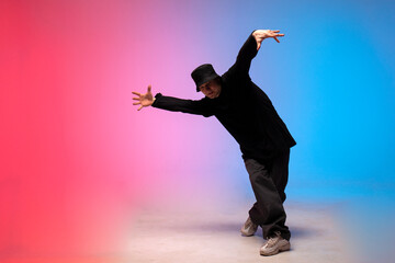 young guy dancer in black clothes break dancing in neon lighting, man performs hip hop movement in...