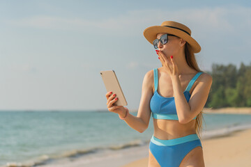 Beautiful caucasian woman using digital tablet at the beach. Female digital nomad working from the beach using her digital tablet. Sexy white woman in bikini. Workcation.