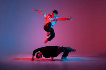 two dancer guys break dance on red blue background and do trick together, male acrobats perform pair dance in neon