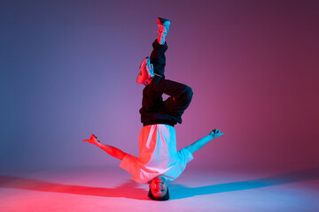 guy hiphop performer break dancing in neon club lighting and doing acrobatic stunt, male dancer stands on his head
