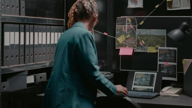 Female detective examining board with clues and research to solve criminal activity, using background checks information in case files. Woman reviewing surveillance photos. Handheld shot.