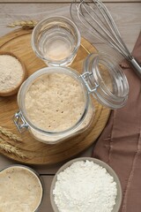 Fototapeta na wymiar Leaven, ears of wheat, whisk, water and flour on beige wooden table, flat lay