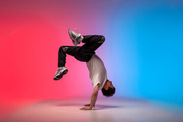young guy dancer is dancing break in neon lighting, male acrobat is doing trick and dance exercise
