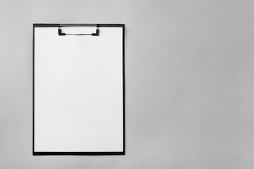 Black clipboard with sheet of blank paper on light grey background, top view. Space for text