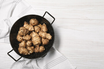 Pan with fresh Jerusalem artichokes on white wooden table, top view. Space for text