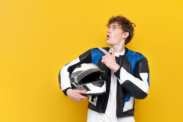 young guy motorcyclist in leather jacket holds helmet and points to the copy space on yellow...