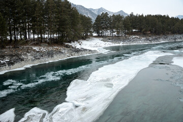 Huge pieces of ice on the thawed bed of a beautiful river flowing through a forested valley in the...