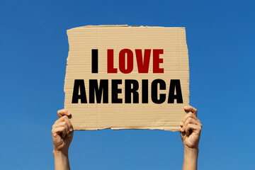 I love America text on box paper held by 2 hands with isolated blue sky background. This message board can be used as business concept about America.