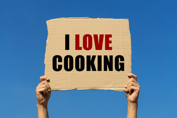 I love cooking text on box paper held by 2 hands with isolated blue sky background. This message...