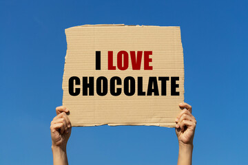 I love chocolate text on box paper held by 2 hands with isolated blue sky background. This message...