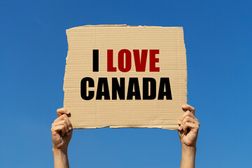I love Canada text on box paper held by 2 hands with isolated blue sky background. This message board can be used as business concept about Canada.