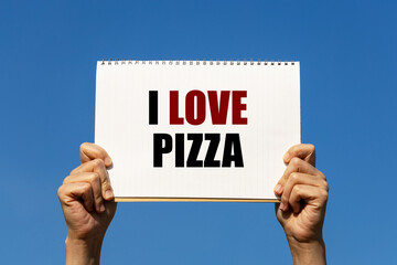 I love pizza text on notebook paper held by 2 hands with isolated blue sky background. This message can be used as business concept about pizza.