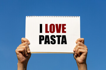 I love pasta text on notebook paper held by 2 hands with isolated blue sky background. This message can be used as business concept about pasta.