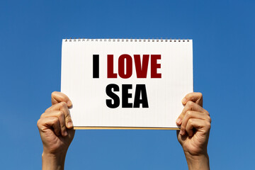 I love sea text on notebook paper held by 2 hands with isolated blue sky background. This message can be used as business concept about sea.