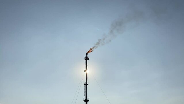 Silhouette or heavily backlit view of oil refiner smoke stack flare 