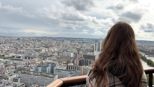 A girl on a eiffel tower looks around at the city of Paris visible houses the Seine River with boats and the city 06.04.22 Paris France center. High quality 4k footage