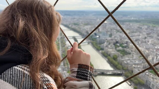 A girl on a eiffel tower looks around at the city of Paris visible houses the Seine River with boats and the city 06.04.22 Paris France center. High quality 4k footage