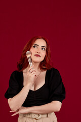 Stylish woman holding make-up brushes while posing against an isolated background.