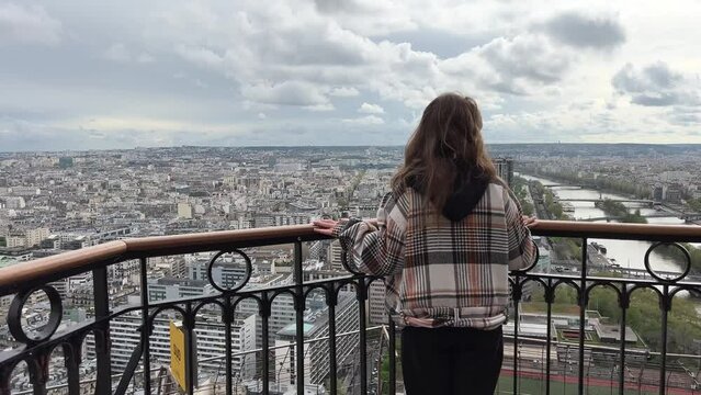 A girl on a eiffel tower looks around at the city of Paris visible houses the Seine River with boats and the city 06.04.22 Paris France center. High quality 4k footage