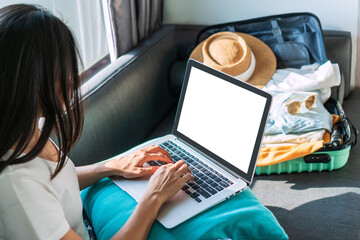Happy young Asian woman planning vacation travel with laptop, reading tourist blog online, booking tickets or hotel room on web, getting ready for summer holiday trip at home. Copy space