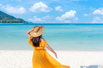 Happy traveler Asian woman on yellow dress relax on the tropical sandy beach. Summer, holiday concept. Copy space