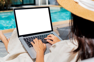 Freelancer using laptop working remotely near swimming pool. Young Asian traveler woman working on computer during her summer holiday. Work from anywhere, Technology and lifestyle concept, copy space