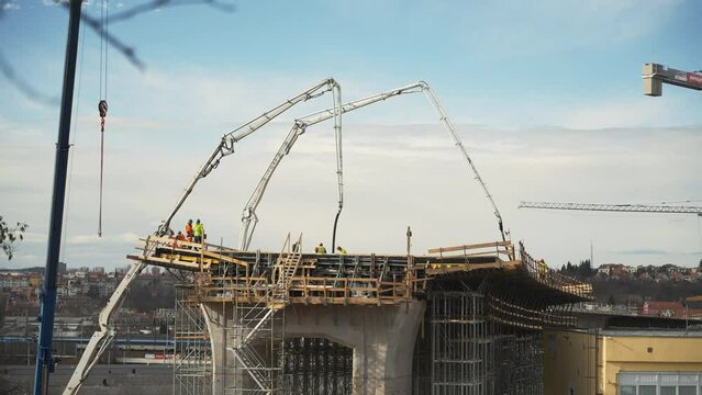 Tall crane concrete pumps and workers at city bridge construction site.