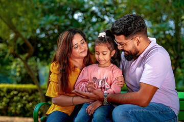 Happy Young indian parents with their cute little daughter sitting at park or garden.