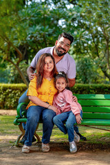Fototapeta premium Happy Young indian parents with their cute little daughter sitting at park or garden.
