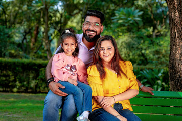 Fototapeta premium Happy Young indian parents with their cute little daughter sitting at park or garden.