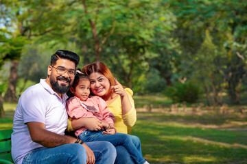 Happy Young indian parents with their cute little daughter sitting at park or garden.