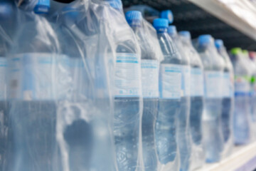 Plastic water bottles in packaging on a shelf in a store. Blurred. Side view.