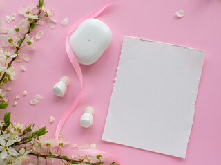 White wireless headphones on pink background with cherry flowers, paper card and copy space. Womens, Valentines and Mothers Day gift. Concept of music and elegance. Buying birthday gifts. 