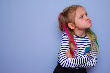 The child is a rebel. A little girl with colored hair and crossed arms on her chest against a gray...