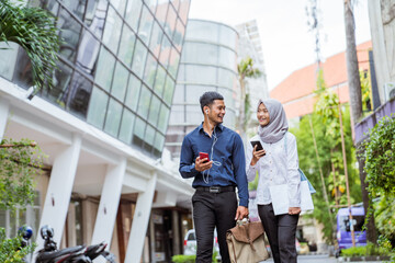 Asian male and female Muslim workers chat while walking to work together between office buildings...