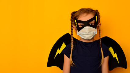 Child in a Superhero costume in a carnival and medical mask with wings behind his back on an orange...